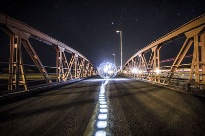 Illuminated bridge over road against sky at night