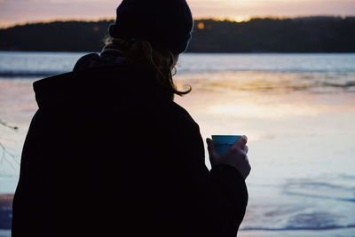 Rear view of woman looking at sea during sunset