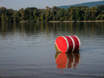 Red tin container  on lake against trees during sunny day