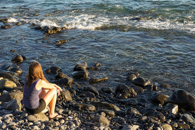 Rear view full length of woman sitting at sea shore