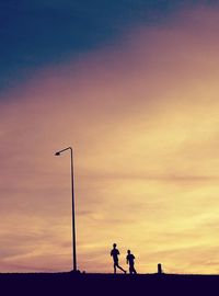 Silhouette people standing on street against orange sky
