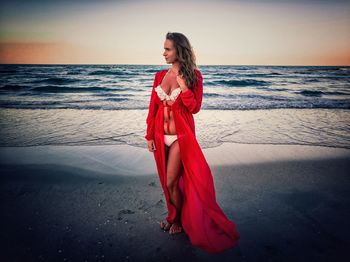 Young woman standing at beach against sky during sunset