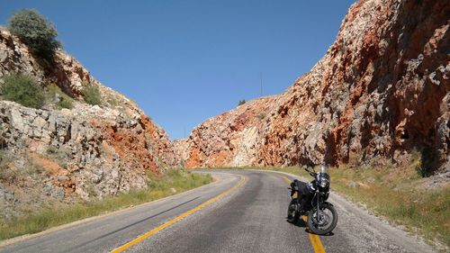 Motorcycle parked on road amidst rocky mountains against clear sky