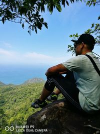 Midsection of man sitting at seaside against sky