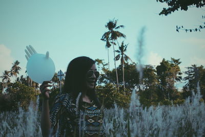 Woman holding glove balloon while standing amidst plants