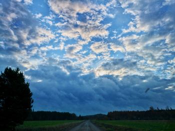 Road passing through field against cloudy sky