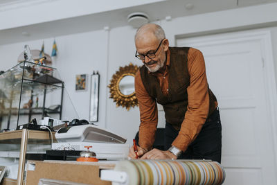 Senior male entrepreneur writing on paper at desk while working in antique shop