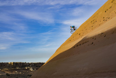 Man on sand dune in desert against cloudy sky