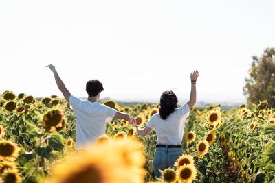 Rear view of couple with arms raised standing on land against sky