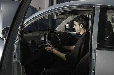 Side view of male technician sitting in automobile and checking information about troubleshooting