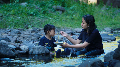Side view of friends sitting on rock by lake