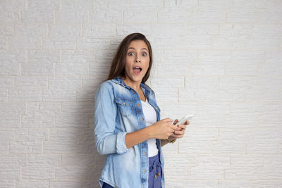 Portrait of young woman using phone while standing against wall