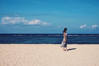 Rear view of woman standing on beach against sky