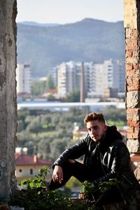 Young man sitting against buildings in city