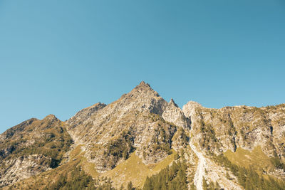 Low angle view of rocky mountains against clear blue sky