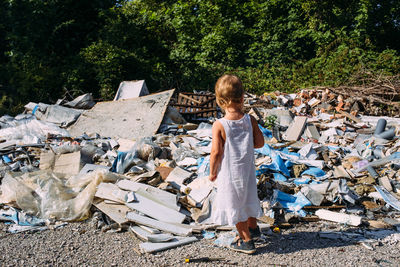 Little girl at a dump among a heap of scattered garbage in the forest.