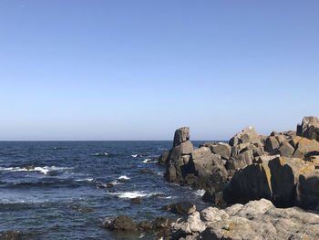 Rocks by sea against clear blue sky