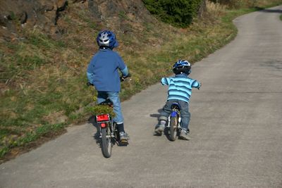 Rear view of siblings cycling on road