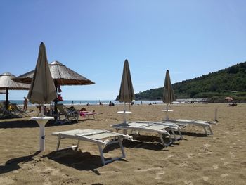 Chairs on beach by sea against clear sky