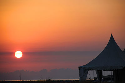 Silhouette tent at beach against orange sun in romantic sky