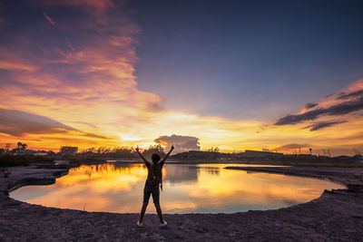 Woman standing by lake against sky during sunset