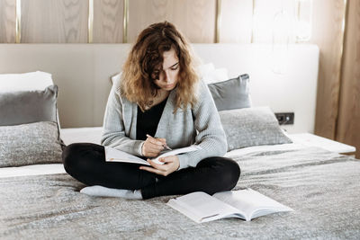 Young woman using laptop while sitting on bed at home