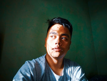 Portrait of young man looking away against wall at home