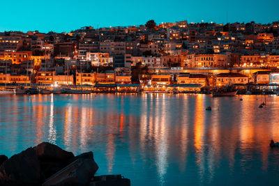 Illuminated buildings by sea against sky at dusk