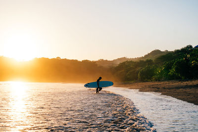 Man surfing in sea against sky during sunset