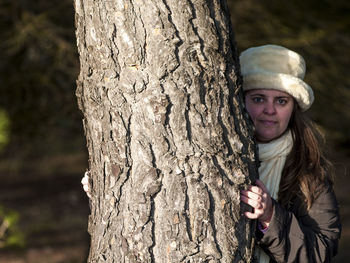 Portrait of mature woman standing behind tree trunk