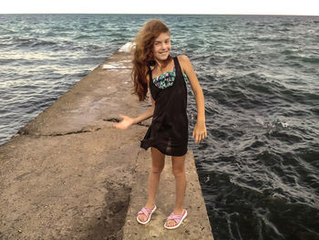 Portrait of happy girl standing on rock over sea