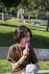 Boy eating sitting on bench while eating ice cream in park during sunny day