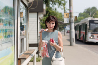 A brunette woman with a red purse on the street outside the store pays goods.