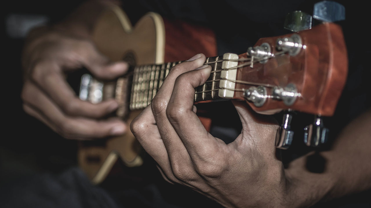 MIDSECTION OF MAN PLAYING GUITAR AT CAMERA