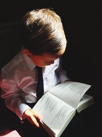 High angle view of boy reading book in sunlight at darkroom