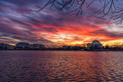 Sea by buildings against sky during sunset