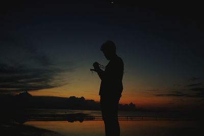 Silhouette man standing on shore against sky during sunset