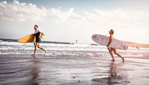 Cheerful couple running on beach with surfboards