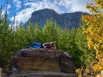 Single  male,model laying on a rock with trees and a mountain background 