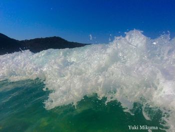 Water splashing in sea against blue sky