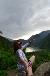 Woman sitting on mountain against sky