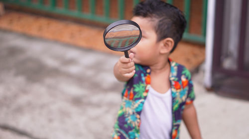  baby boy holding magnifying glass while standing on road