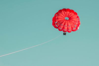 Low angle view of people paragliding against clear sky