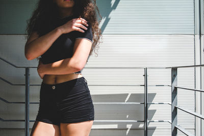 Midsection of woman in black shorts standing by railing on sunny day
