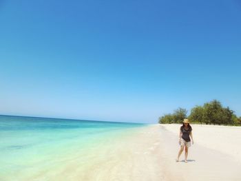 Woman walking on shore at beach against clear sky