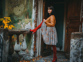 Full length portrait of woman standing outside abandoned house