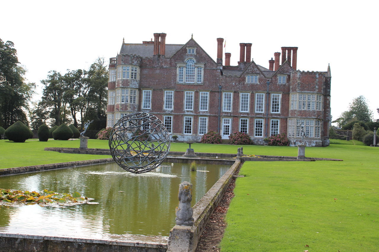 architecture, building exterior, built structure, grass, tree, green color, clear sky, water, sky, fountain, lawn, growth, plant, day, statue, outdoors, pond, sculpture, park - man made space, sunlight