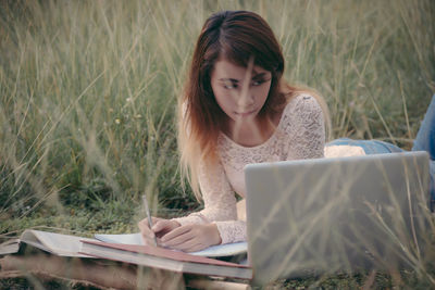 Young woman looking away while studying on field