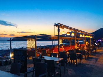 Illuminated restaurant by sea against sky at sunset