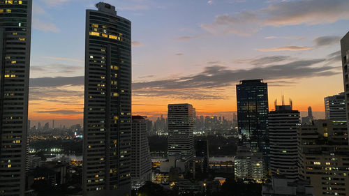 Illuminated buildings in city against sky at sunset